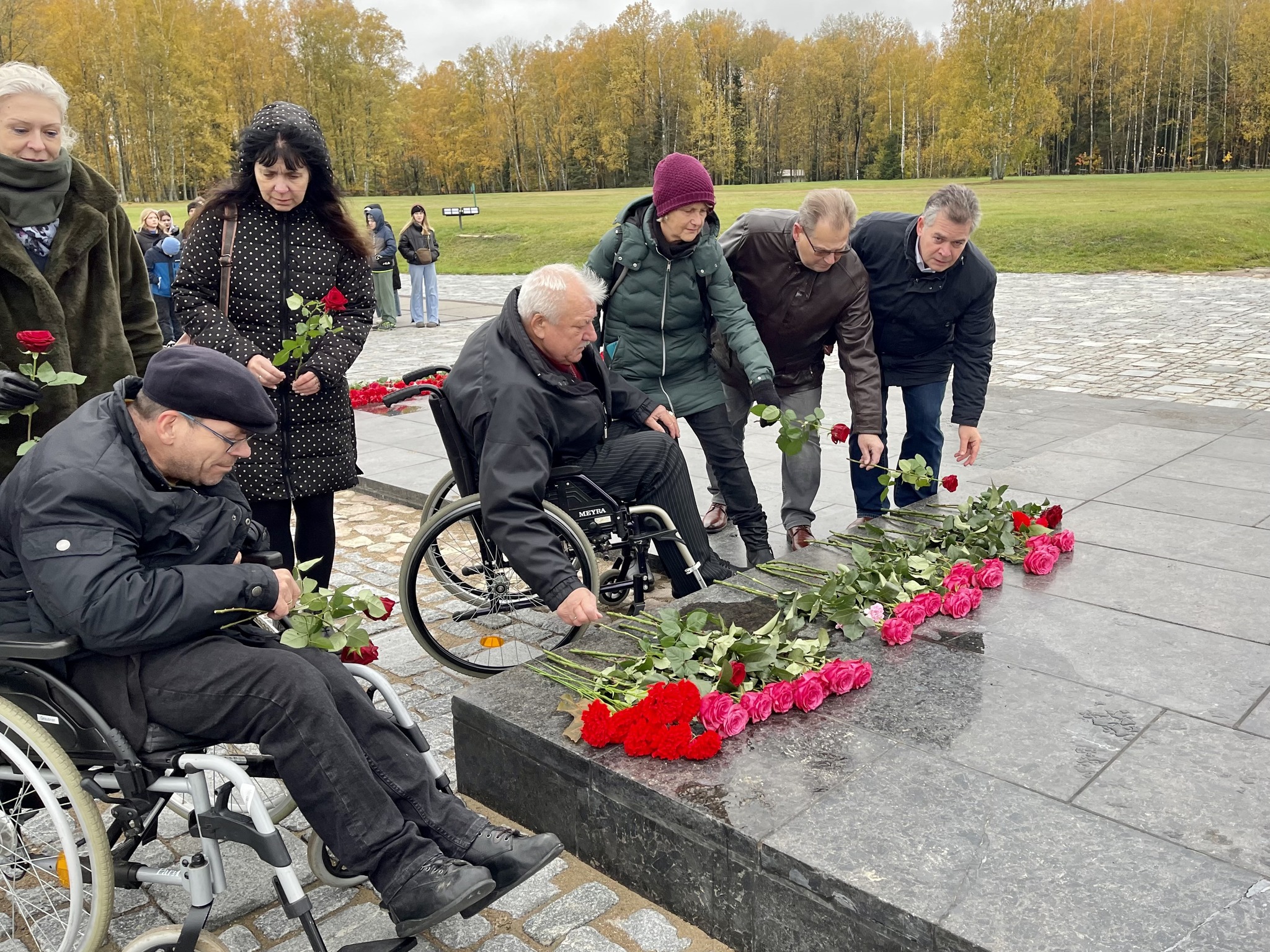 Bild zeigt mehrere personen die eine rose auf ein denkmal niederlegen.